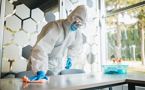 Man in biohazard gear wiping down desk in school