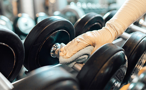 Dumbbell being wiped down with gray shammy in gym setting